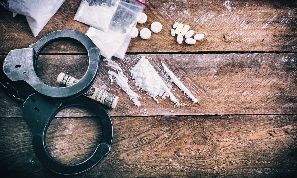 Drug Crime Defense Attorneys Topeka Kansas portrayed by assorted drugs and handcuffs spread on a wooden table.